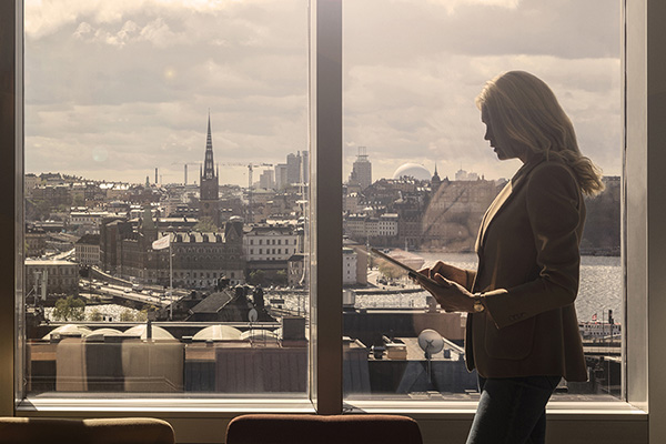 En affärskvinna som står med sin dator vid ett fönster i starkt solljus.